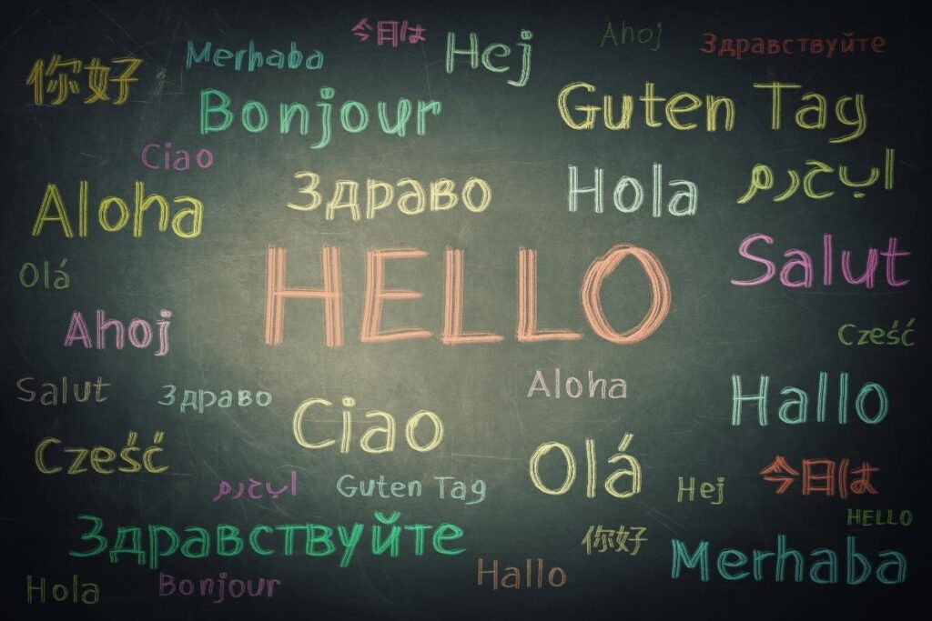 A chalkboard displays “HELLO” in large orange letters at the center, surrounded by “hello” written in various languages—such as Bonjour, Hola, Aloha, Hallo, Salut, Ciao, and others—in different colors and fonts.