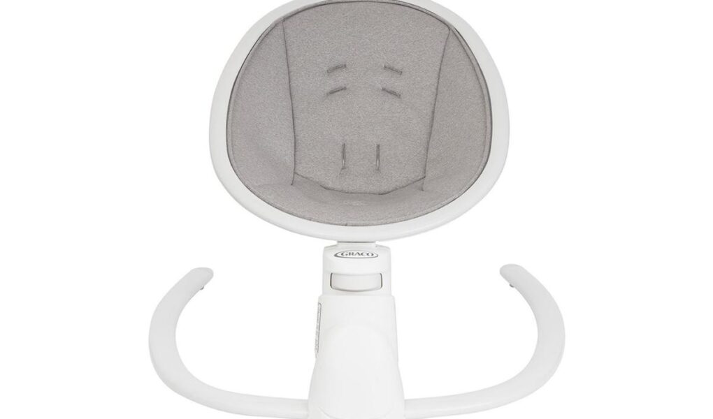 A top-down view of a modern baby rocker seat with a white frame and light gray padded fabric inside. The seat has built-in harness slots and two curved white legs extending forward, designed for stability and gentle rocking.