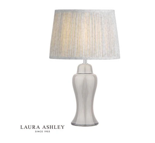 A sleek, silver table lamp with a glossy, curved base and a pleated, light grey fabric lampshade. The Laura Ashley logo and the text "Since 1953" appear in the bottom left corner against a white background.